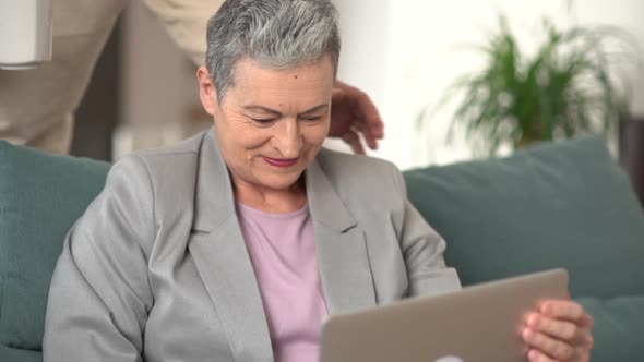 Mature Woman with Short Gray Hair is Working with Laptop While Sitting on Sofa at Home