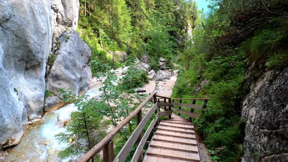 POV shot of someone walking down wooden stairs in a beautiful canyon. Next to the stairs is a wild r