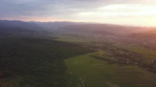 Aerial view of Nadvirna town with scattered houses and distant Carpathian mountain hills at sunset.