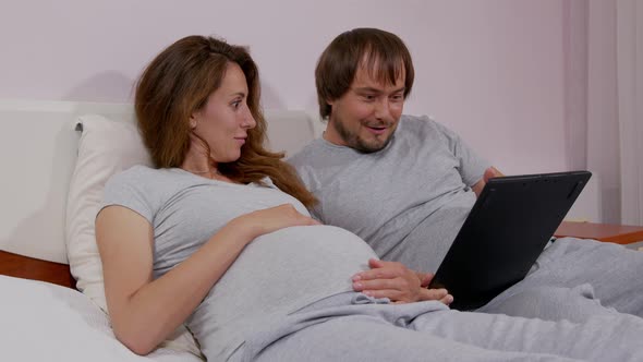 Happy Man and His Pregnant Wife with Smartphones at Home. Pregnancy, Technology and People Concept.