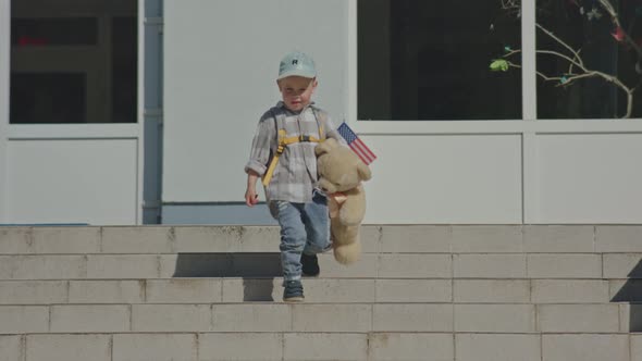Child Kid Boy in Cap Backpack USA Flag and Teddy Bear Walking Building Stairs
