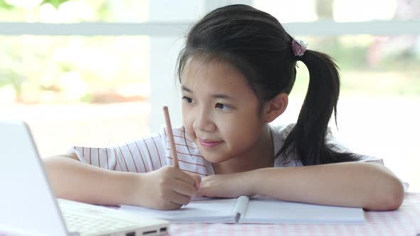 Beautiful Asian Girl Thinking And Writing To Notebook On The Tablet