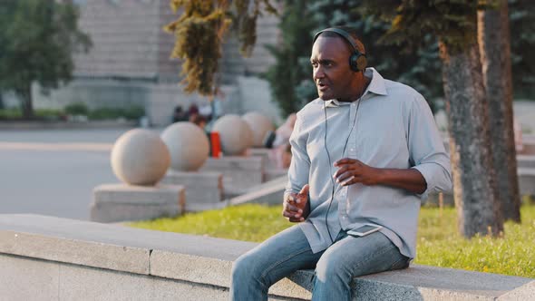 Happy Carefree Black Emotional Senior African American Man Sitting Outdoors Listening Song in