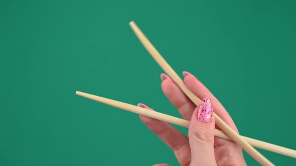 Female Hands Hold Japanese Chopsticks For Sushi Rolls on Green Background