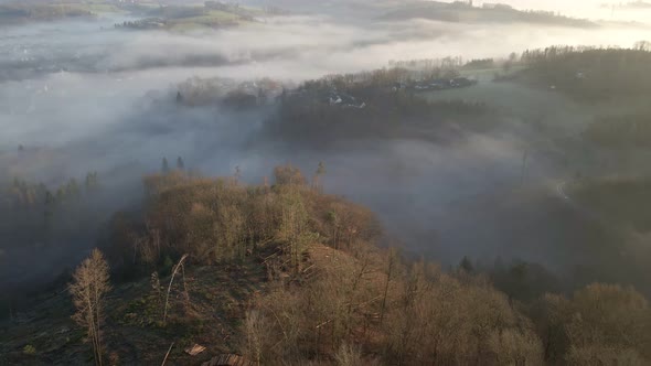 Thick morning fog floating through the valleys of North Rhine-Westphalia, Germany. Aerial backwards