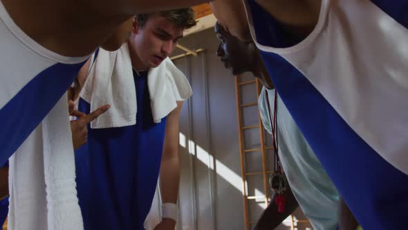 Diverse male basketball team and coach in huddle discussing game tactics