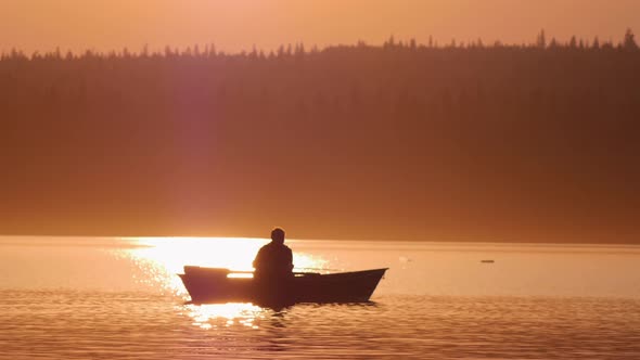 Man Sitting in a Boat on River and Fishing on Sunset