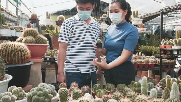 Two masked asian people talk about the cacti plants in front of them on a table at a nursery greenho