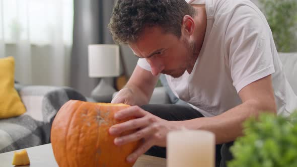 Young Man Cuts Out Jack's Lantern with a Knife at Home