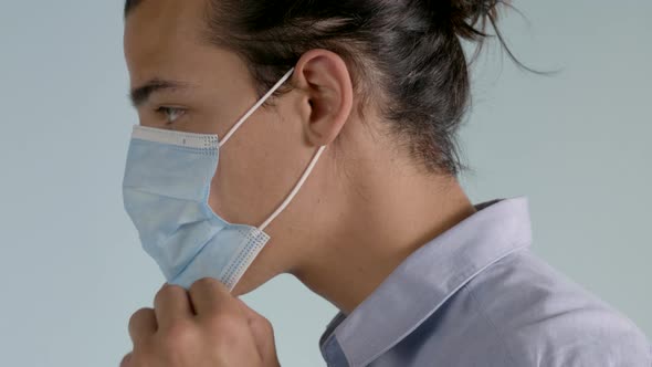 Left Profile of Adult Male with Long Hair Wearing Button Down Shirt puts on a Surgical Mask on a Neu