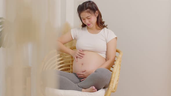 Happy Pregnant Woman sitting on bed holding and stroking her big belly at home