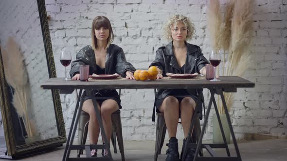 Wide Shot Portrait of Two Confident Caucasian Women with Serious Facial Expression Sitting at Table