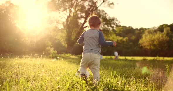 Boy Standing with a Soccer Ball in the Summer Running on the Field with Grass Rear View