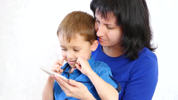 Happy Mother and Her Son Use a Smartphone for Games on a White Background, Smiling and Having Fun