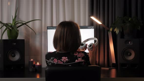 Woman putting on headphones sitting at office desk.