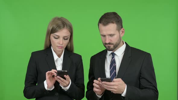 Male and Female Business Professionals Using Smart Phones Against Chroma Key