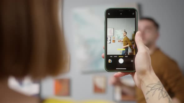 Young Couple Hanging Picture on Wall Woman Making Video on Smartphone How Man Hangs Framed Picture