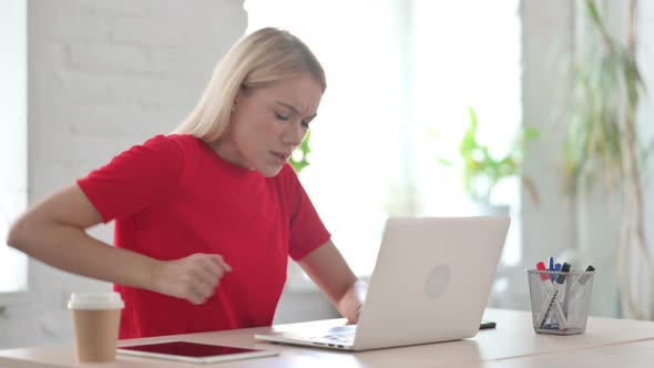 Young Blonde Woman having Back Pain while using Laptop in Office