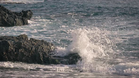 Waves crash against rocks along the shore and splash into the air. Slow motion view of the power of