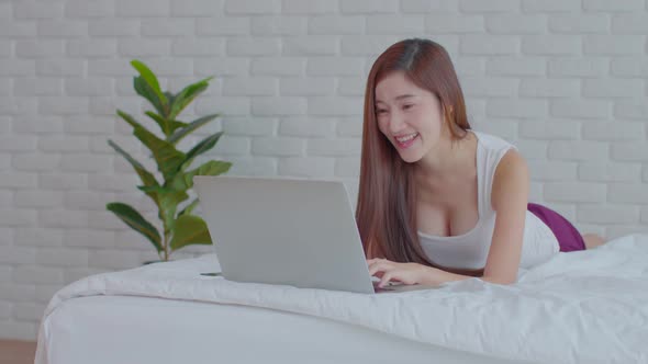 Asian young woman lying on bed and using computer laptop for using social media and shopping online