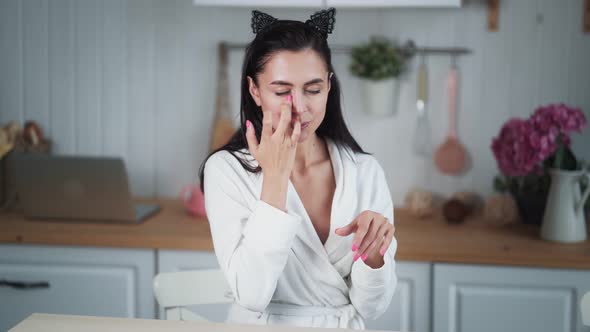 Young Woman in Bathrobe Applies Cream on Her Face and Does Facial Massage