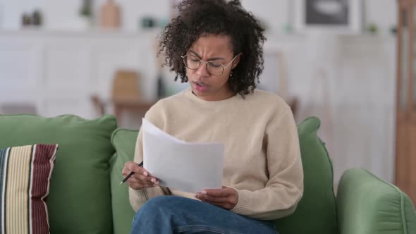 African Woman with Documents Reacting to Loss on Sofa