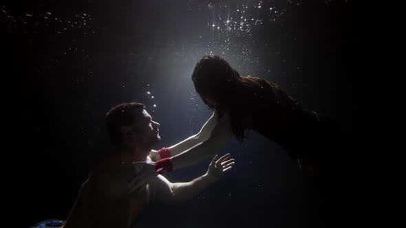 Loving Pair is Floating Underwater in Darkness Stretching Hands to Each Other