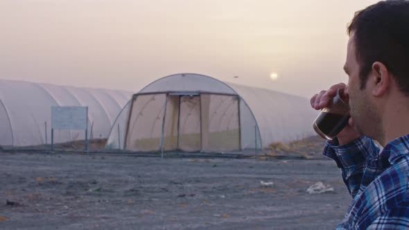 Farmer drinking coffee looking at the sunrise over a greenhouse farm