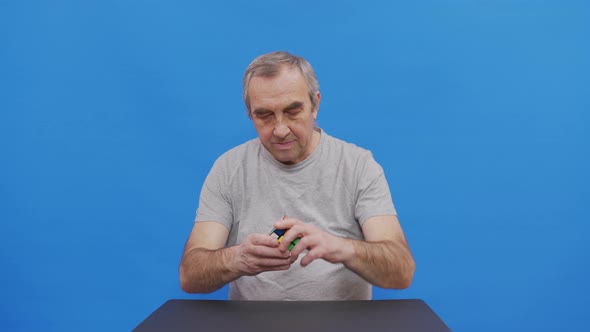 A Elderly Man Solving Rubik. Isolated on Blue.