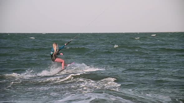 Young Adult Caucasian Woman in Good Shape Enjoys Riding a Kiteboard for Surfing Doing Extreme Tricks