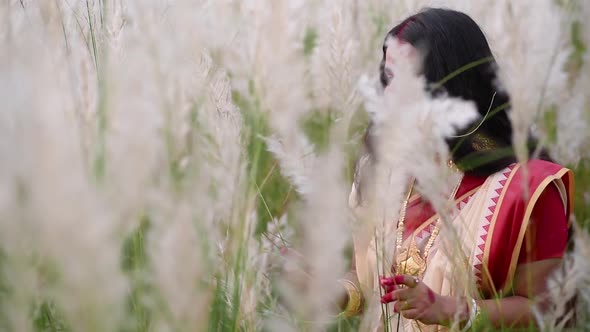 A happy and playful married Indian bengali woman wearing saree plays with the long white grass in a