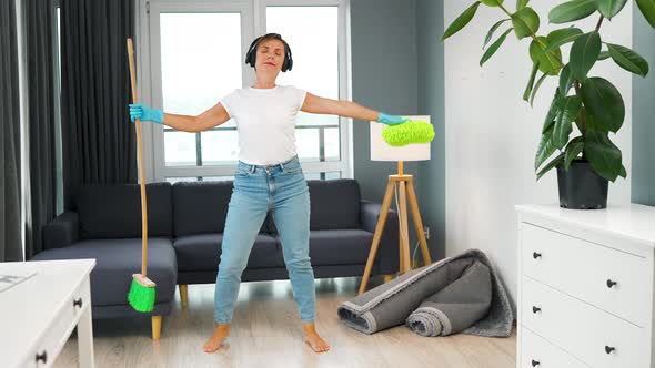 Woman in Headphones Cleaning the House and Having Fun Dancing with a Broom and Washcloth