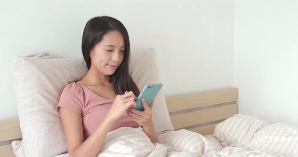 Woman using smart phone on bed 