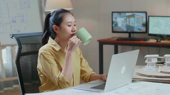 Asian Woman Engineer Drinking Coffee While Using A Laptop To Work At The Office