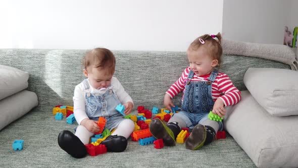 Two baby girls, playing with toys on the sofa at home