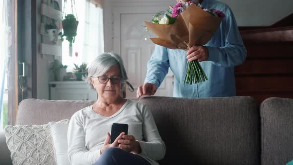 Portrait of couple of two happy and in love seniors or mature and old people holding flowers at home