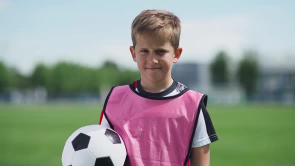 Portrait of a Football Player Boy, a Young Boy Stands Near a Football Field and Looks at the Camera