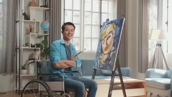 Asian Artist Man In Wheelchair Turn To Cross His Arms And Smile While Painting A Girl On The Canvas