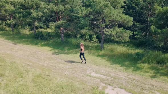 Aerial Shot, Tracking: Young Pretty Girl Goes in for Sports in the Morning, Runs Along Pine Forest.