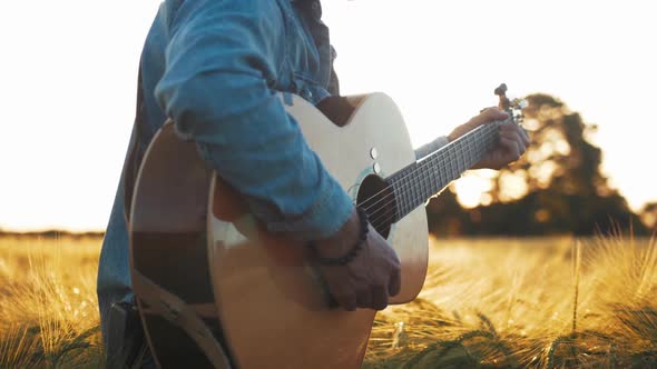 Musician playing guitar in field at sunset golden hour slow motion