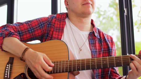 Young Man Playing Guitar Sitting on Windowsill