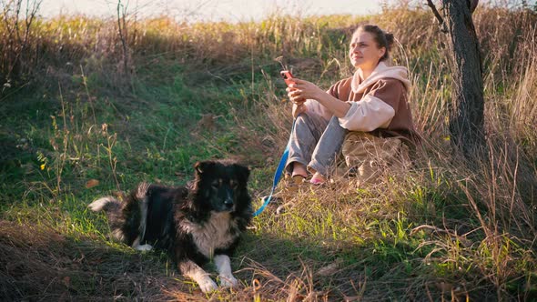A Young Adult Woman Using Her Phone While Walking with Her Dog