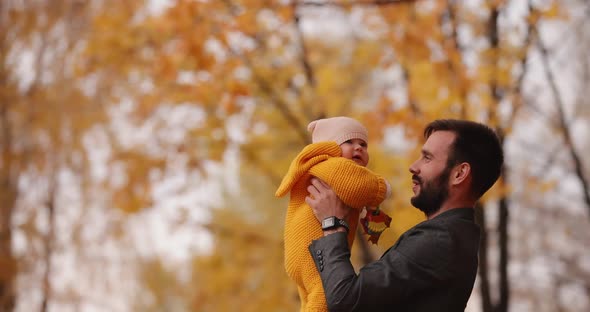 Happy Dad Throws and Catch His Little Baby at the Autumn Park