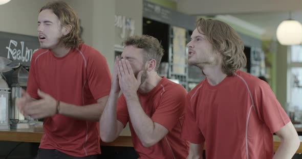 Male friends watching TV in pub making various gestures