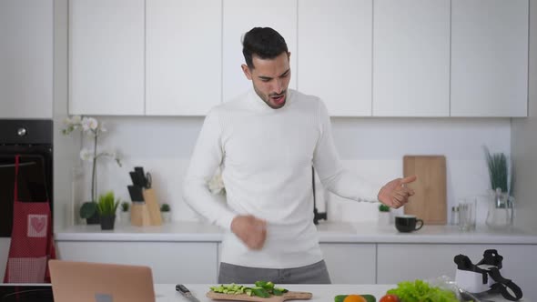 Cheerful Young Middle Eastern Man Imitating Guitar and Drums Playing Cooking Healthful Vegan Salad