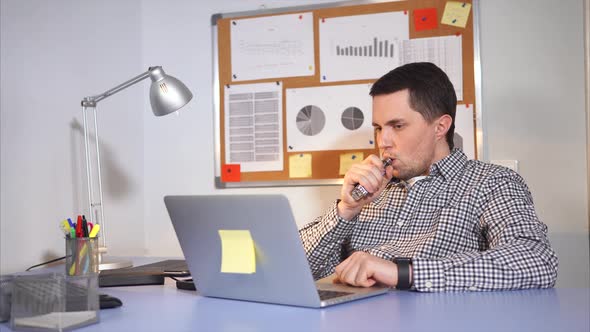 Young Man Smoking an Electronic Cigarette or Vaping in the Office.