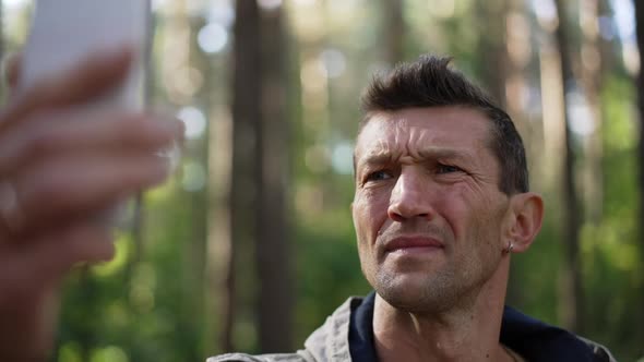 Closeup Unsure Anxious Worried Caucasian Man with Smartphone Standing in Sunny Forest Outdoors