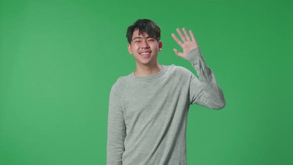 An Asian Man Waving Hand And Smiling While Standing On Green Screen In The Studio