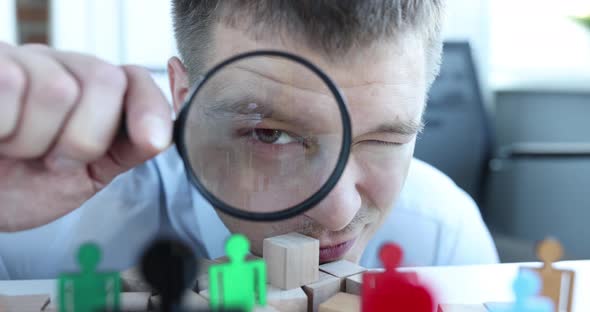 Man Looking at Figurines of Multicolored Men Through Magnifying Glass  Movie