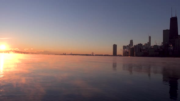 Sun rising over Lake Michigan horizon over Chicago downtown skyline in winter with sea smoke in wate